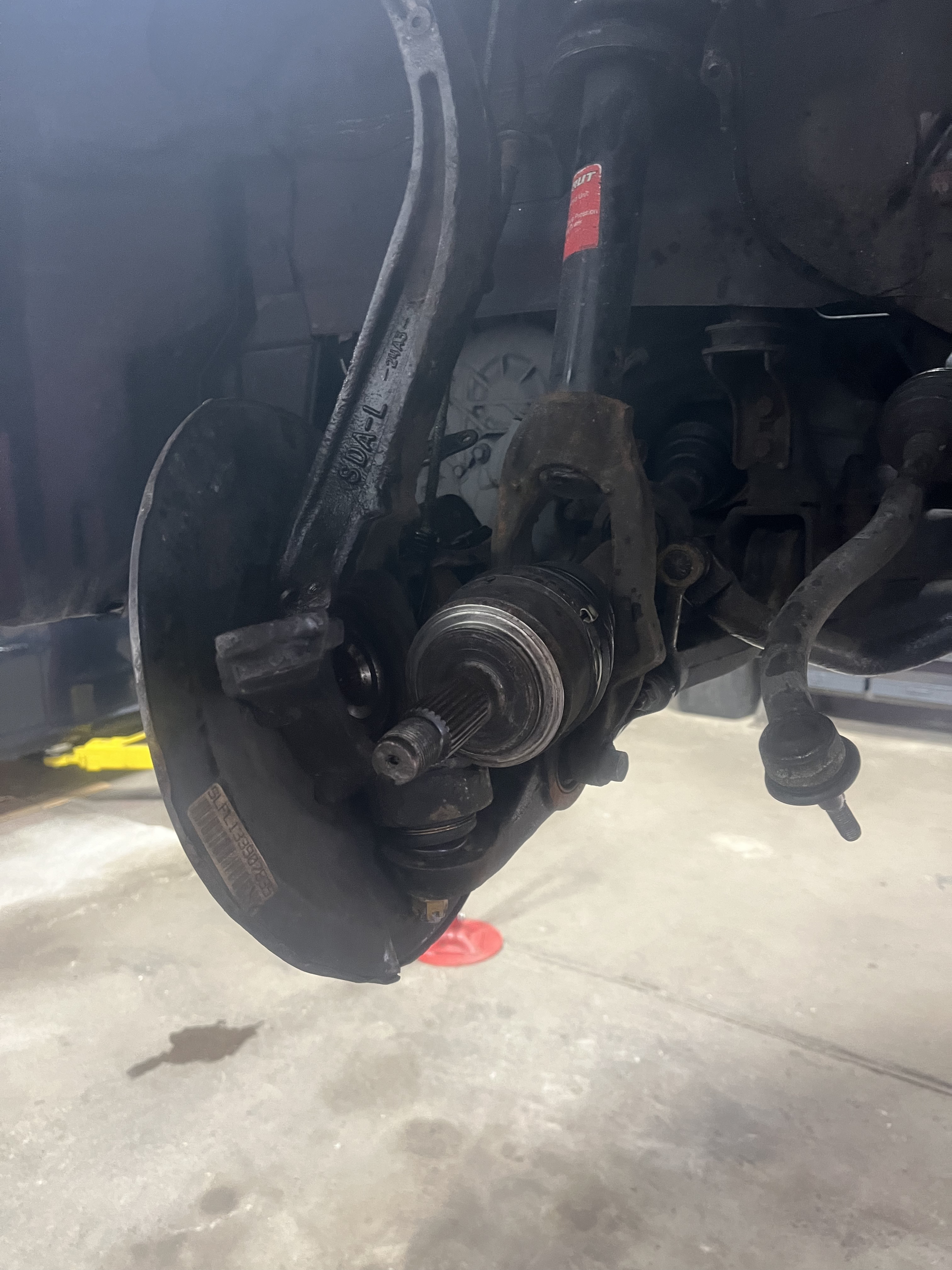 Honda Accord front suspension underbody view with CV axle and dust shield visible during bearing service