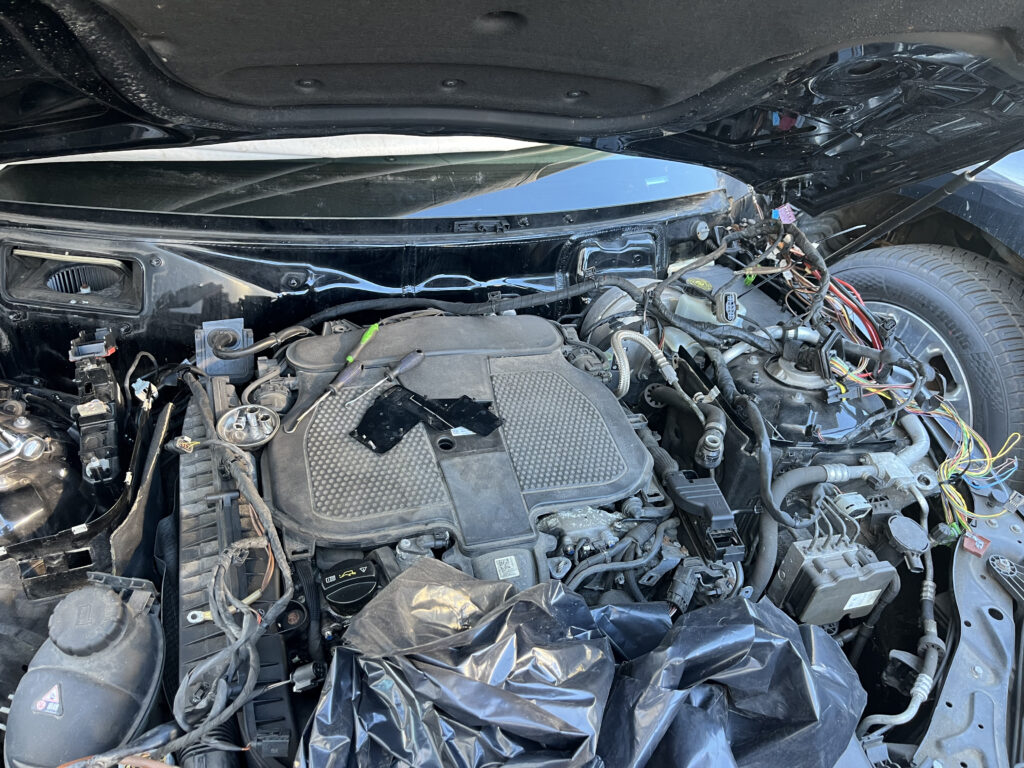 Mercedes-Benz C-Class engine bay with hood and front end open, engine cover visible, wiring harness pulled to the side during replacement