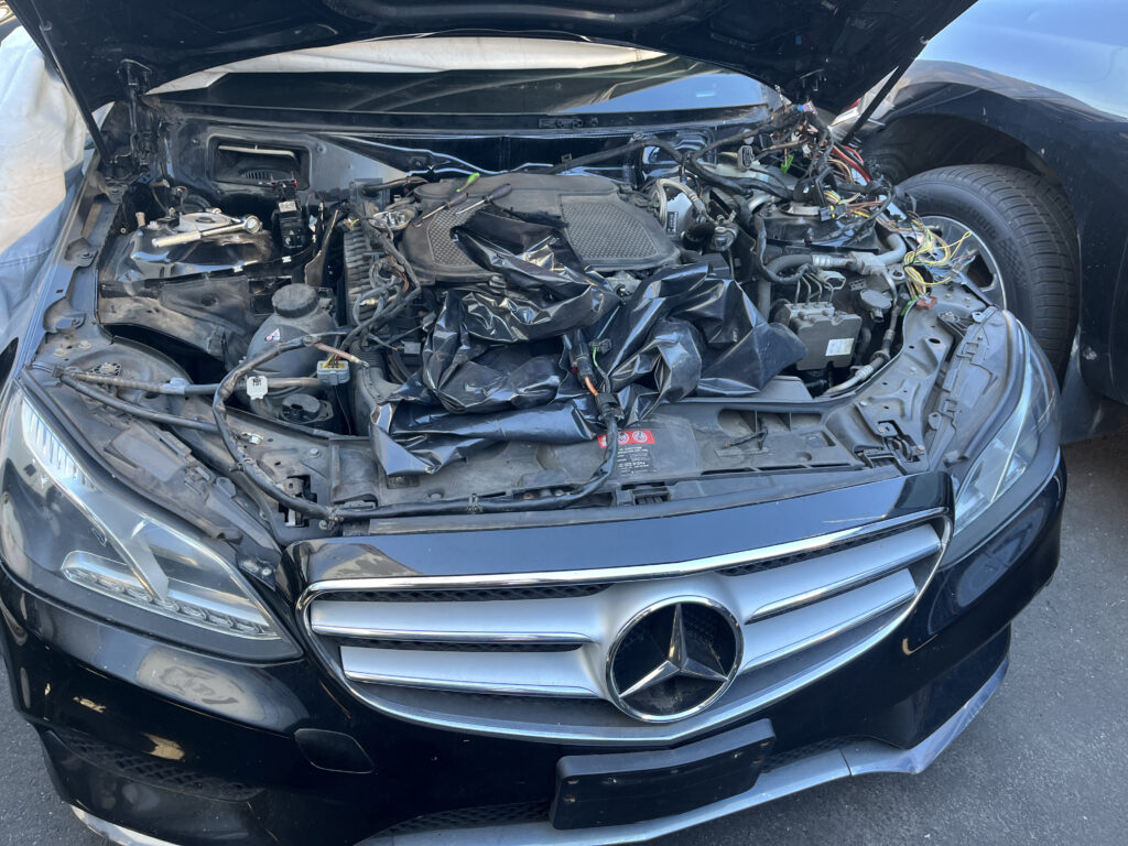 Front view of black Mercedes-Benz C-Class with Mercedes star grille visible, hood up showing engine bay during wiring harness service in Philadelphia