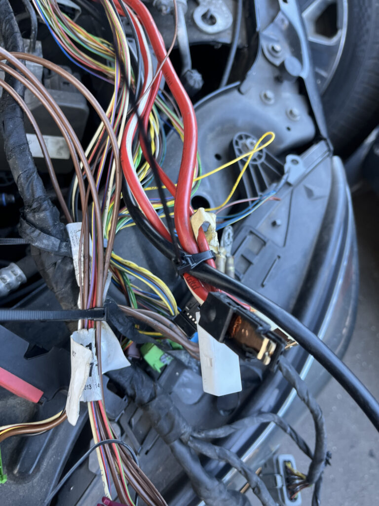 Close-up of removed Mercedes-Benz wiring harness showing damaged multi-color wires and red power cable spread out for inspection